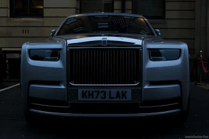 A luxury car parked in a quiet city car park at dawn, photographed head-on, with dark reflections and early morning light accentuating its broad grille and imposing front.