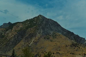 A rugged mountain peak rising above a dry, rocky landscape beneath a blue sky with scattered clouds.
