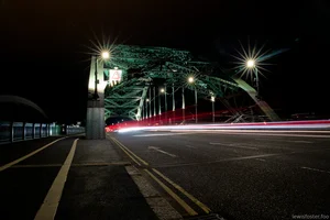 A long exposure photograph of Wearmouth Bridge in Sunderland at night, with light trails from passing vehicles.